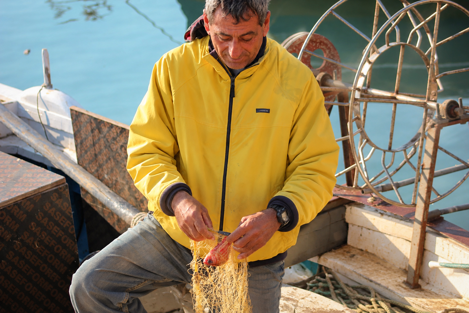 Un pêcheur en veste jaune qui démêle un filet sur sa barque