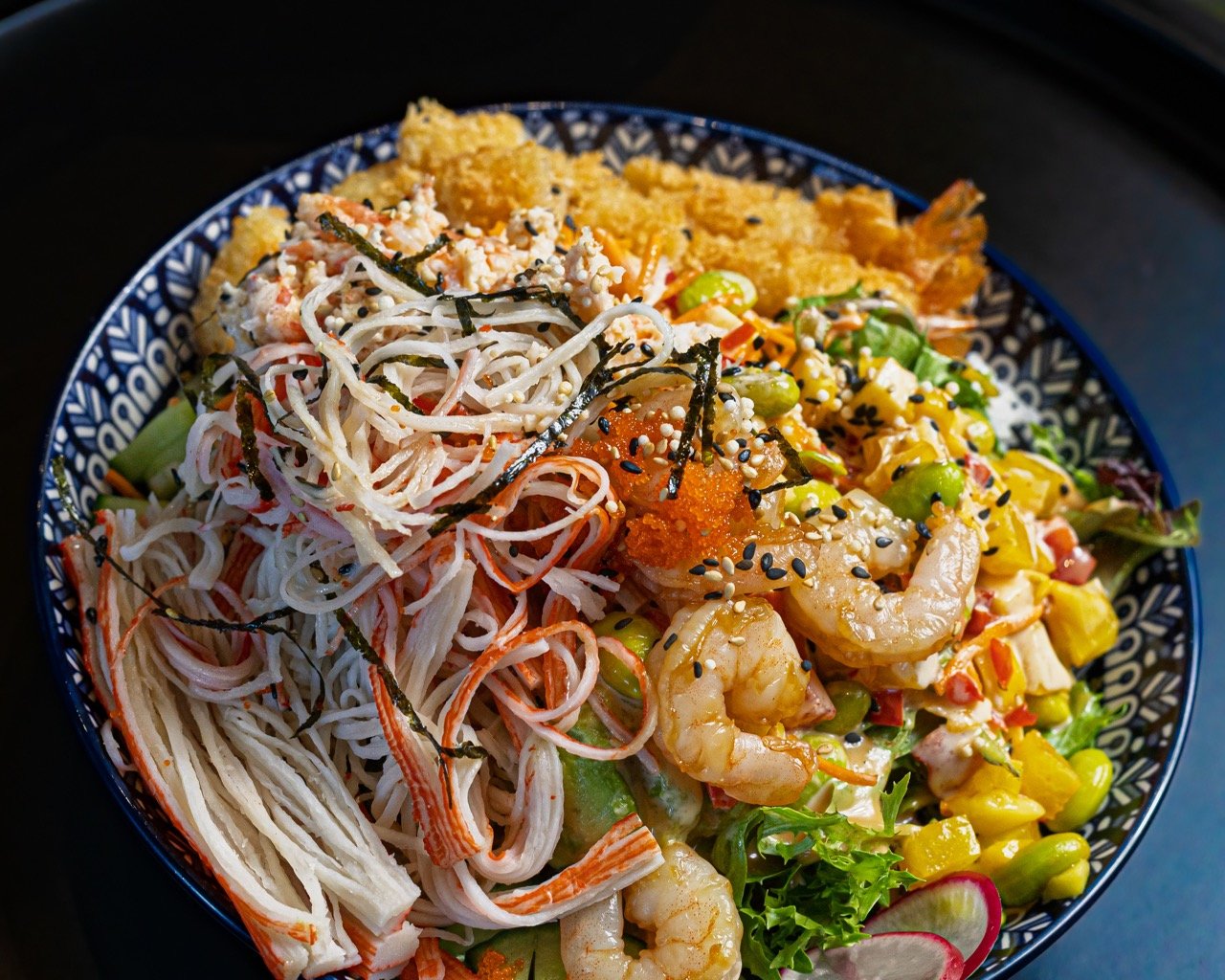 A woman happily eating from a vibrant bowl of modern fusion food.